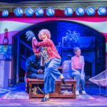 Dame Maureen Lipman as Allegra dancing while Bailey Patrick as Officer Rogers and Elizabeth Bower as Anna watch from the cottage sitting room.
