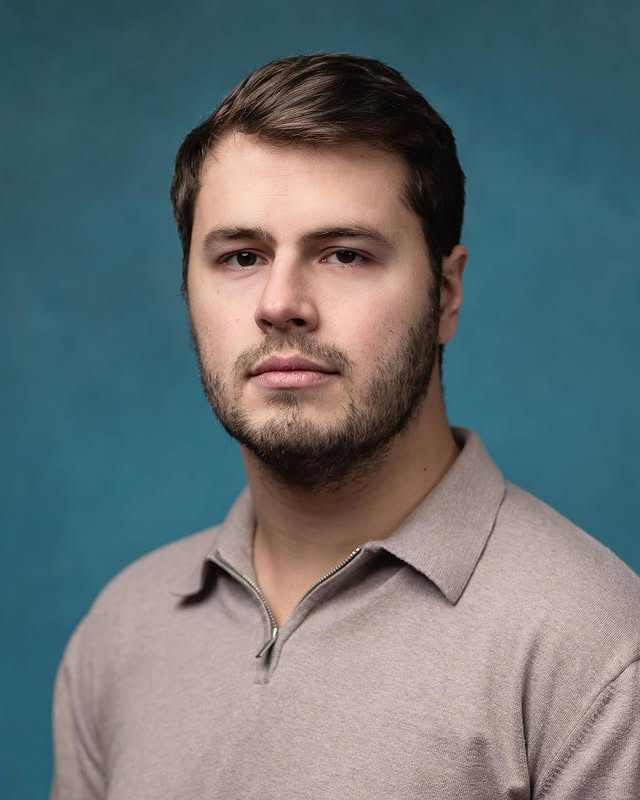 Portrait headshot of Thomas Carruthers against a blue-green background